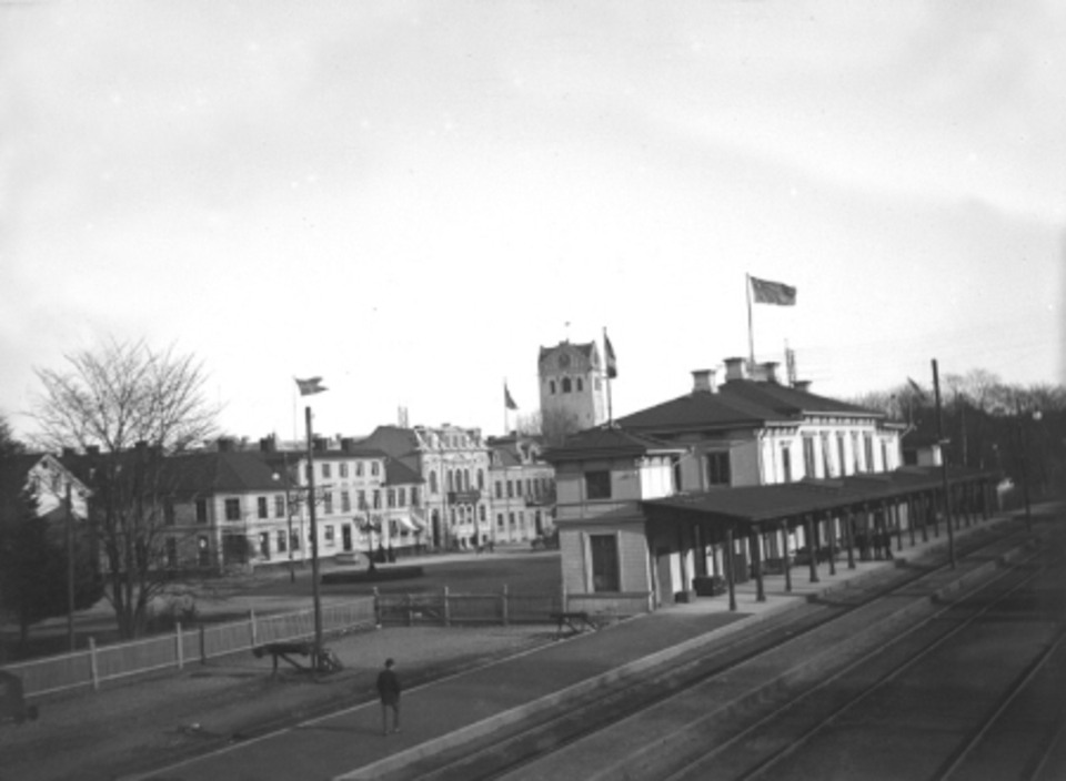 Människor sover. Det är en tidig morgon i Växjö men stadens unionsflagga är hissad. Kanske är det en stor dag som stundar? Bakom stationen syns husen vid Norra järnvägsgatan (kvarteret Linné).