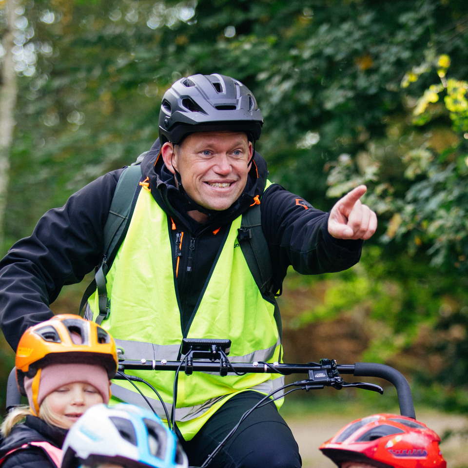 En manlig förskolelärare som cyklar med tre barn.