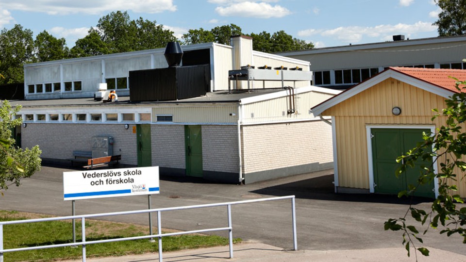 Vit tegelbyggnad med gröna dörrar. Framför byggnaden står en skylt med texten Vederslövs skola och förskola