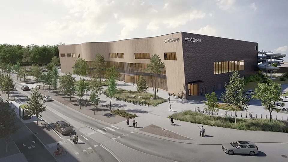 Visualisering av den planerade Växjö simhall på Bäckaslövsområdet, sedd från gatan mittemot den nya domstolsbyggnaden. Byggnaden har en ljus träfasad med inslag av mörk tegel, omgiven av träd, gång- och cykelvägar samt människor som rör sig i området.